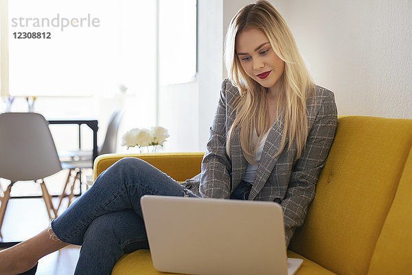 Geschäftsfrau auf gelber Couch sitzend  mit Laptop