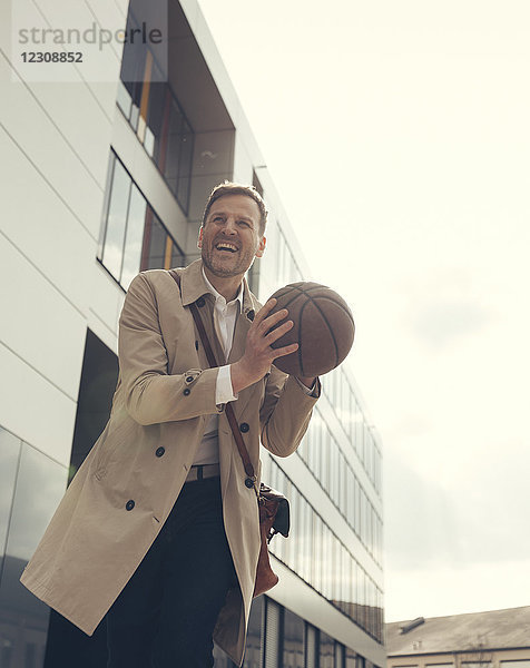 Glücklicher Geschäftsmann beim Basketballspielen vor dem Bürogebäude
