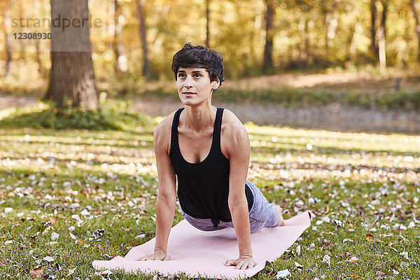 Mittlere erwachsene Frau im Wald praktiziert Yoga  Cobra-Pose