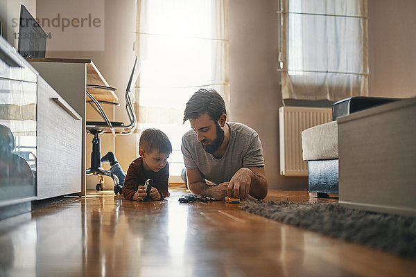 Vater und Sohn liegen zusammen auf dem Boden und spielen mit Spielzeugautos.