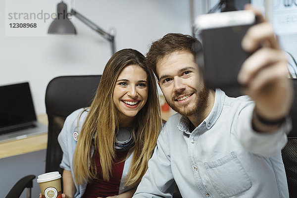 Zwei lächelnde Gelegenheitskollegen im Büro  die einen Selfie nehmen