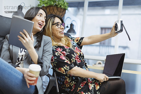 Zwei glückliche junge Frauen im Büro  die einen Selfie nehmen.