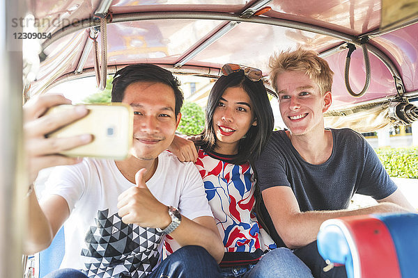 Thailand  Bangkok  drei Freunde auf Tuk Tuk Tuk  die Selfie mit Smartphone fahren