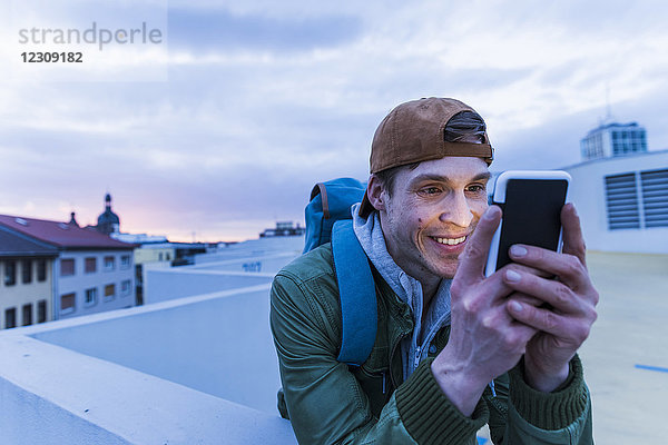 Lächelnder Mann schaut in der Abenddämmerung auf leuchtendes Smartphone