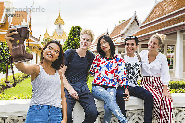 Thailand  Bangkok  fünf Freunde  die Selfie mit Smartphone vor dem Tempelkomplex nehmen