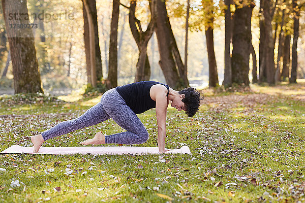 Mittlere erwachsene Frau im Wald praktiziert Yoga  Kletterübung
