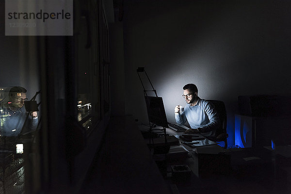 Geschäftsmann mit Tasse Kaffee arbeitet nachts am Computer im Büro