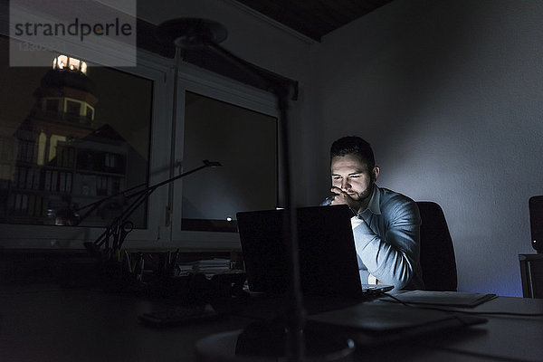 Geschäftsmann bei der Arbeit am Laptop im Büro bei Nacht