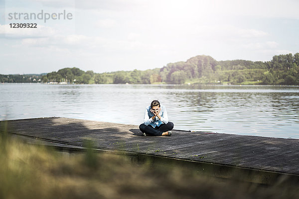 Entspannte Frau sitzt auf einem Steg am See