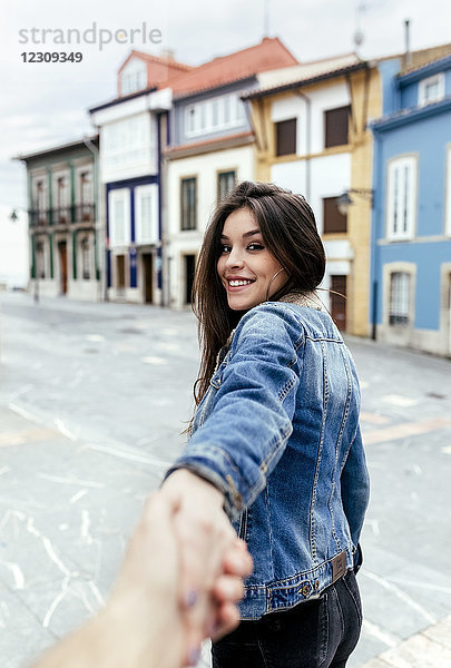 Porträt einer lächelnden  brünetten Frau  die in einer Stadt die Hand hält.