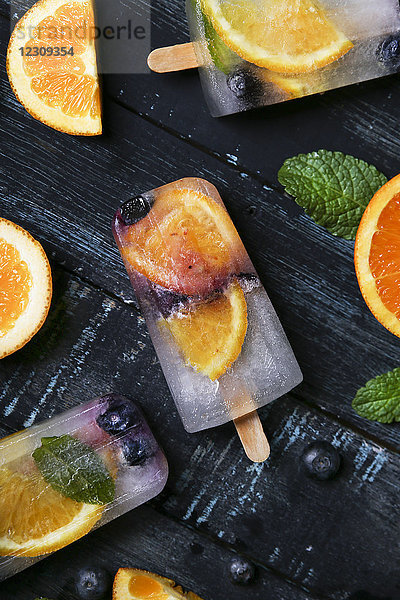 Hausgemachte Entgiftungs-Popsicles mit Heidelbeeren  Orangenscheiben und Minzeblättern auf schwarzem Holz