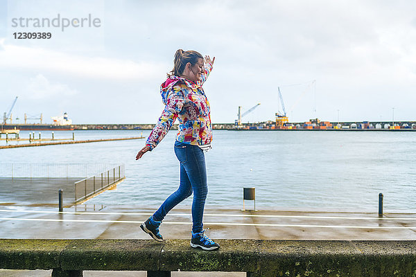 Azoren  Sao Miguel  Frau  die auf einer Steinbank im Hafen von Ponta Delgada spazieren geht.