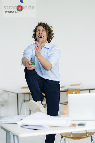Lachender Geschäftsmann jongliert mit Bällen in seinem Büro