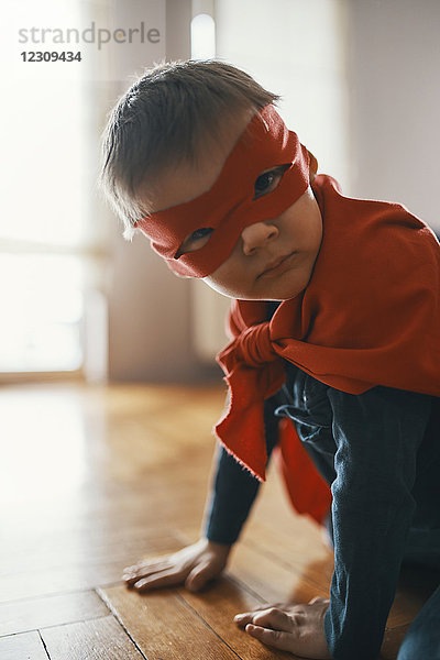 Kleiner Junge verkleidet als Superheld  der zu Hause auf dem Boden hockt.