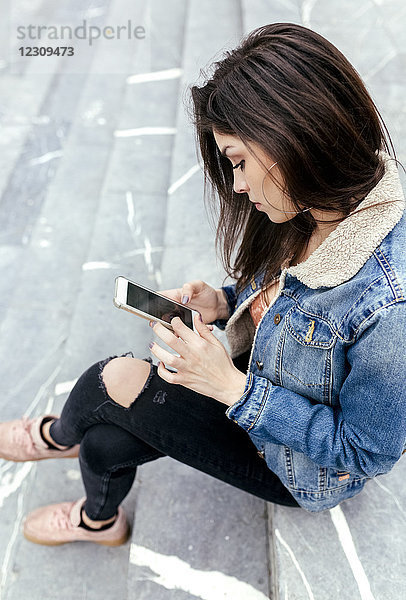 Junge Frau sitzt auf einer Treppe und überprüft ihr Smartphone.