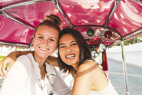 Thailand  Bangkok  Portrait von zwei glücklichen Freunden auf Tuk Tuk Tuk