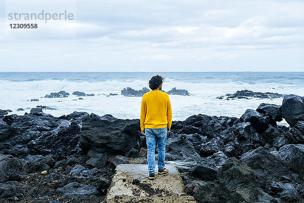 Azoren  Sao Miguel  Rückansicht des Menschen mit Blick auf das Meer von der steinigen Küste aus