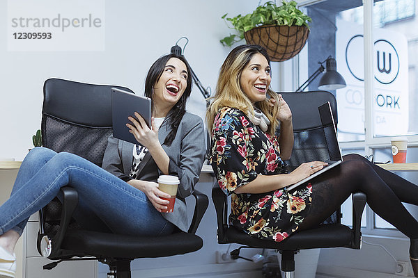 Zwei glückliche junge Frauen im Büro mit Laptop und Tablett