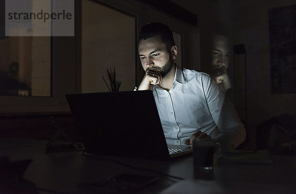 Geschäftsmann bei der Arbeit am Laptop im Büro bei Nacht