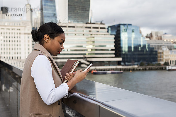 UK  London  Geschäftsfrau auf der Brücke stehend mit Handy