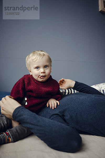 Vater und Sohn ruhen auf der Couch  Baby sitzt auf dem Gesicht des Vaters.