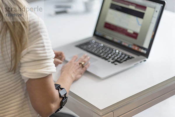 Frau mit tragbarem Arm mit Laptop am Schreibtisch