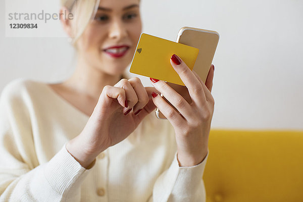 Frau mit Smartphone und Bankkarte zu Hause