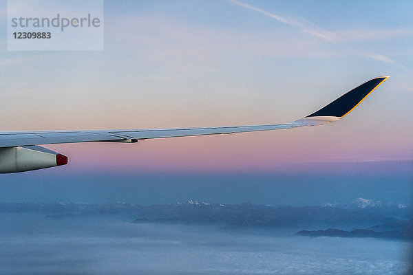 Flügel eines Flugzeuges über den Wolken mit Bergen im Hintergrund