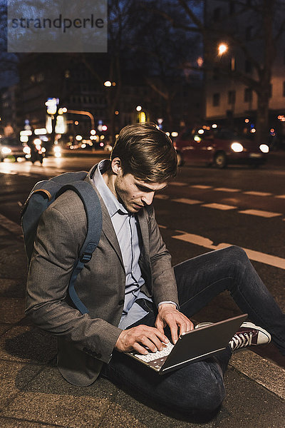 Geschäftsmann mit Laptop in der Stadt bei Nacht