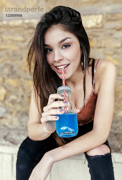 Porträt einer lächelnden brünetten Frau beim Trinken von blauer Limonade