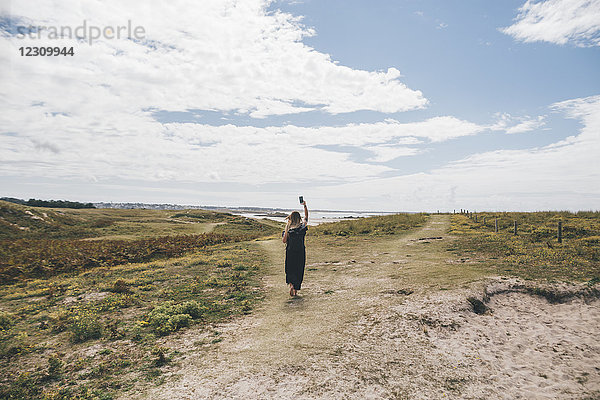Frankreich  Bretagne  Landeda  Dunes de Sainte-Marguerite  junge Frau  die auf der Düne an der Küste mit Handy läuft