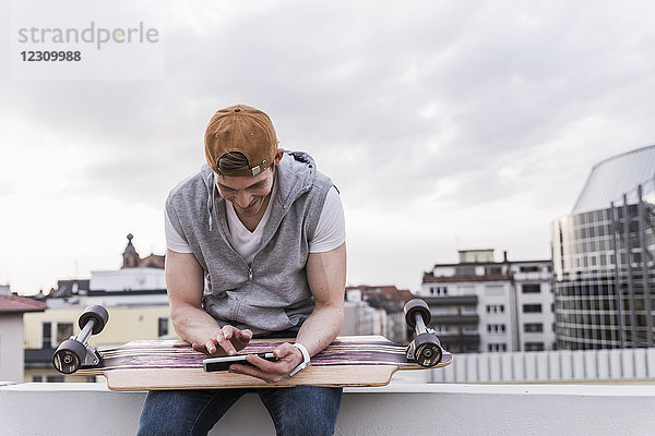 Lächelnder Mann sitzt in der Stadt mit Skateboard per Handy