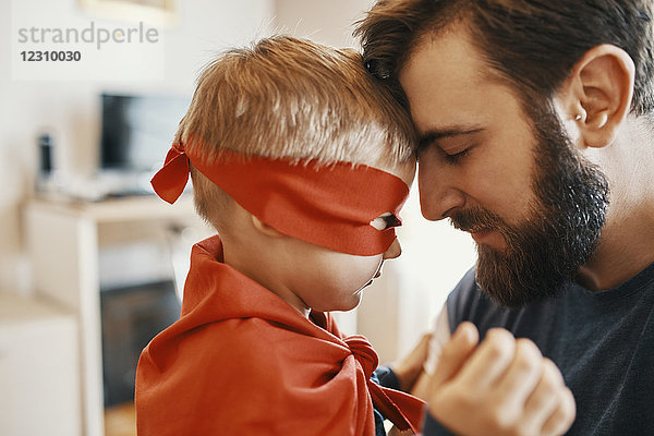 Kleiner Junge verkleidet als Superheld Kopf an Kopf mit seinem Vater.