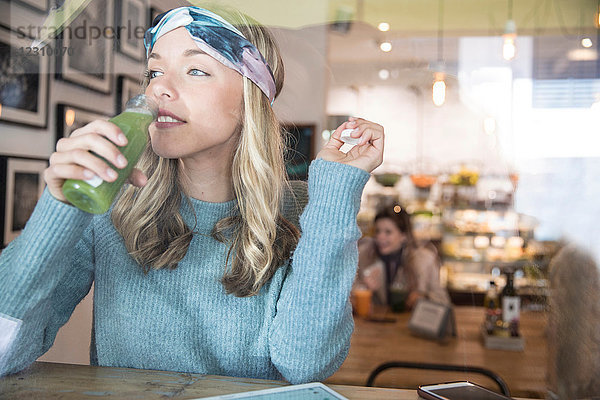 Junge Frau trinkt Gemüsesaft am Fensterplatz eines Cafés