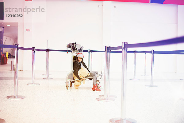 Porträt eines Mädchens  das auf einem Gepäckwagen in der Abflughalle des Flughafens sitzt
