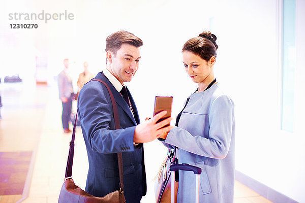 Junge Geschäftsfrau und Mann am Flughafen schauen auf Smartphone
