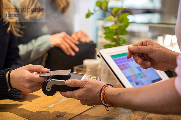Weibliche Kundin im Geschäft  die Waren mit Kreditkarte am kontaktlosen Bezahlautomaten bezahlt  Mittelteil  Nahaufnahme