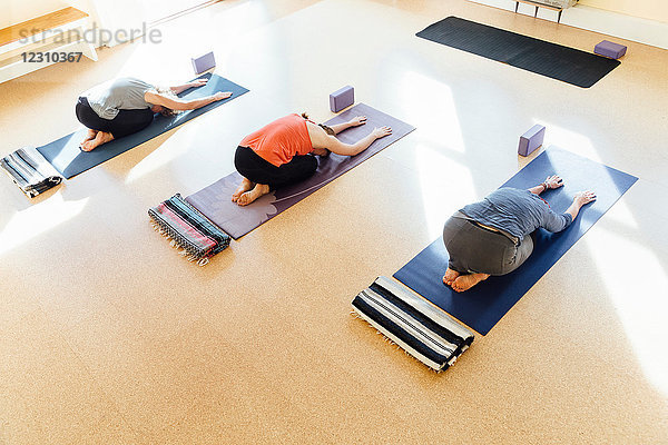 Drei Frauen üben Balasana (Kinderhaltung) im Yogastudio