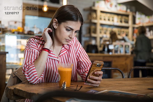 Junge Frau sitzt im Cafe  benutzt Smartphone  Smoothie auf dem Tisch vor ihr