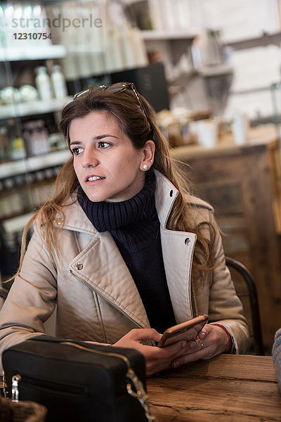 Junge Frau am Cafe-Tisch mit Smartphone in der Hand