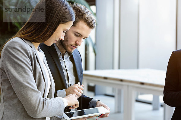 Junge Geschäftsfrau und Mann im Büro schauen auf digitales Tablet