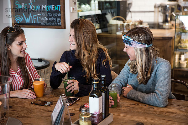 Drei junge Freundinnen mit Gemüsesaft beim Plaudern im Café