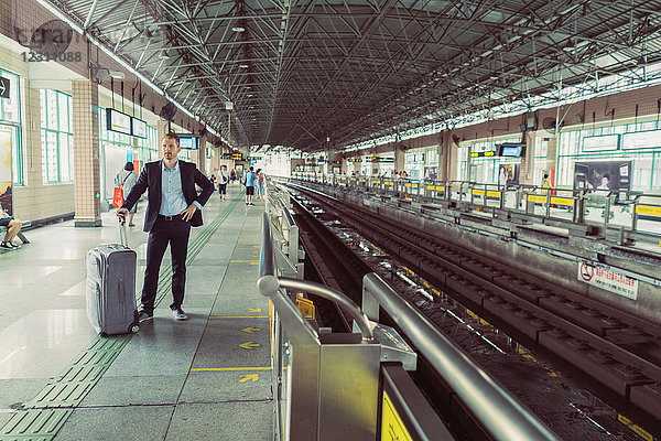 Geschäftsmann mit Rollkoffer  steht am Bahnhof und wartet auf den Zug