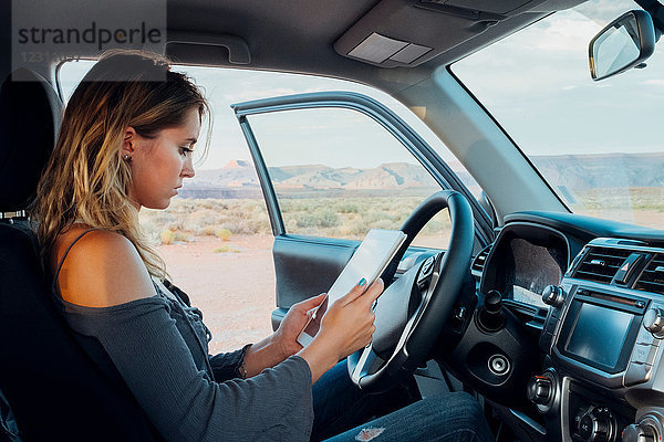 Junge Frau sitzt im Fahrzeug und schaut auf ein digitales Tablet  Mexican Hat  Utah  USA