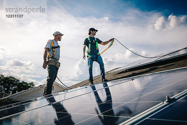 Zwei Handwerker installieren Sonnenkollektoren auf dem Hausdach  Blickwinkel gering