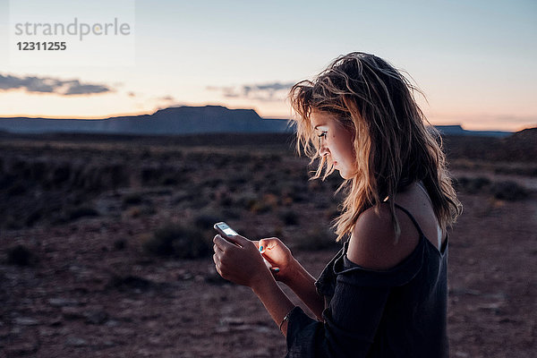 Junge Frau in abgelegener Umgebung  die ein Smartphone benutzt  Mexican Hat  Utah  USA