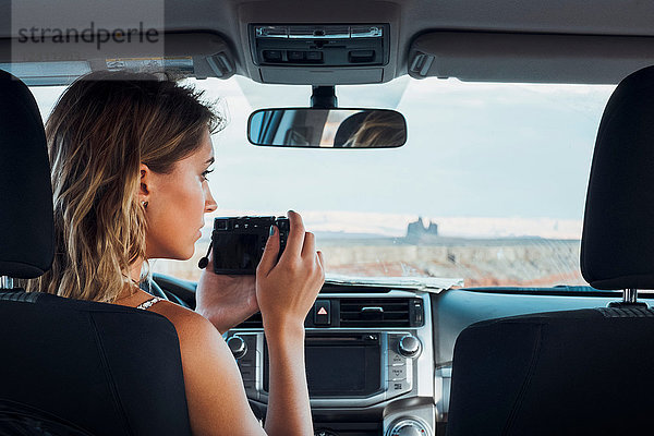 Junge Frau sitzt in einem Fahrzeug  fotografiert durch die Windschutzscheibe  mit Kamera  Mexican Hat  Utah  USA