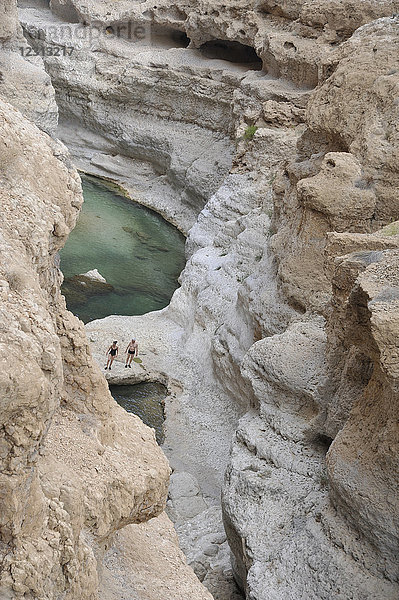 Sultanat Oman  Wadi Shab  2 Personen wandern in einer Schlucht mit türkisblauem Wasser  die von Kalksteinfelsen umgeben ist