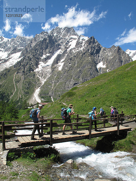 Italien  Aosta-Tal  Ferret-Tal  Courmayeur  eine Gruppe von Wanderern überquert einen Bach auf dem Tour du Mont Blanc Weg vor der italienischen Seite des Mont Blanc Gebirges