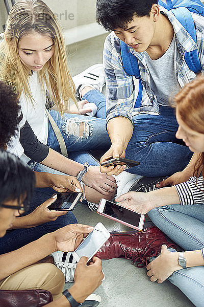 Gruppe von Studenten  die zusammen auf dem Boden sitzen und auf ihre Smartphones schauen